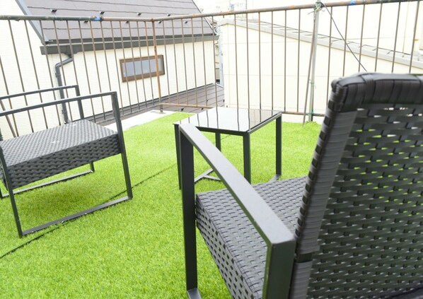 A patio area with a small table and two chairs, surrounded by artificial grass.