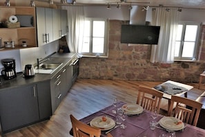 Eine moderne Küche mit Steinwand, einem Essbereich mit Tisch für zwei Personen und einem an der Wand montierten Flachbildfernseher.
