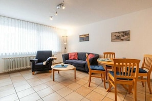 Ein Wohnzimmer mit einer Couch, Sesseln, einem Couchtisch und einem Esstisch.