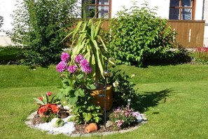 Ein Garten mit vielfältigen Pflanzen und Blumen, einer Holzkiste als Pflanzgefäß und einer kleinen Zierkonstruktion.
