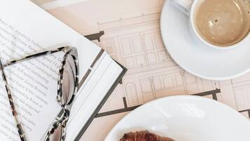 A croissant on a plate, a cup of coffee, a pair of glasses, and a book with text on a table.
