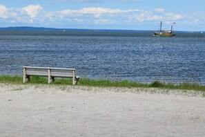 A bench by a calm body of water with a boat in the distance. - Holiday home in Altwarp with swimming pool (Altwarp)