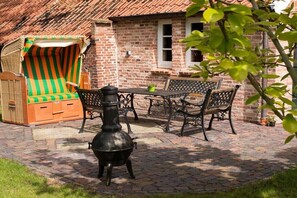 Eine Terrasse mit Ziegelmauer, einem Metallkocher, einem gestreiften Stuhl und einem Tisch mit Stühlen.