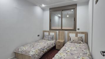 A bedroom with two beds, a window with blinds, a wooden headboard, and a marble floor.