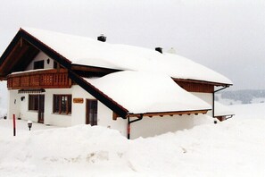 Ein mit Schnee bedecktes Chalet mit geneigtem Dach, einer Holzbalkonage und einem gut sichtbaren Eingang.