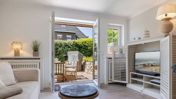 An open door leading to a patio with outdoor furniture, a sofa, a TV stand, and a lamp inside a room. - Beach Love Sylt - Westerland (Westerland)
