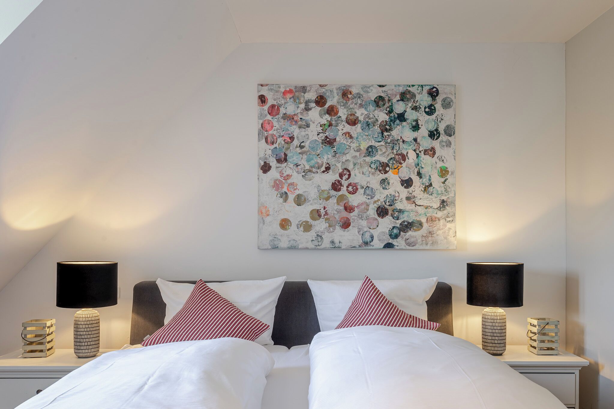 Ein Schlafzimmer mit einem Bett, zwei Nachttischen, Lampen und einem Wandbild.