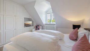 A bedroom with a sloped ceiling, a window with a view, white furniture, and a number '5' on the wall. - Beach Love Sylt - Westerland (Westerland)