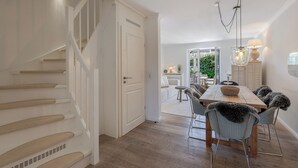 A staircase leading to a dining area with a wooden table and chairs, a hanging light fixture, and a view of an outdoor patio. - Beach Love Sylt - Westerland (Westerland)