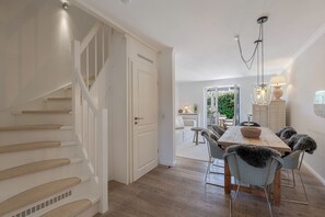 A staircase leading to a dining area with a wooden table and chairs, a hanging light fixture, and a view of an outdoor patio. - Beach Love Sylt - Westerland (Westerland)