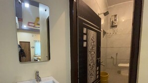 Une salle de bain avec un lavabo blanc, un miroir, une douche et des toilettes.