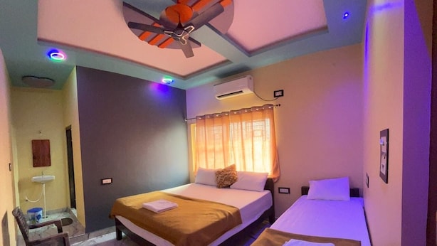 Une chambre d’hôtel avec deux lits, un ventilateur de plafond, un appareil de climatisation, un petit bureau avec une chaise et une fenêtre avec des rideaux.