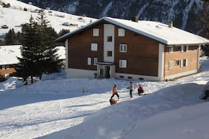 Ein hölzernes Gebäude mit geneigtem Dach, umgeben von verschneiter Landschaft und Bergen.