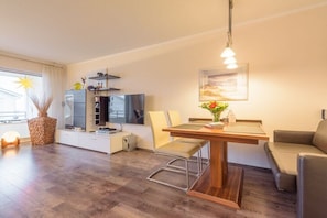 Ein modernes Wohnzimmer mit Esstisch, Sofa, Fernseher und Dekorationselementen.