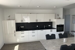 Eine moderne Küche mit weißen Schränken, schwarzen Arbeitsflächen und einem Essbereich mit Tisch und Stühlen.