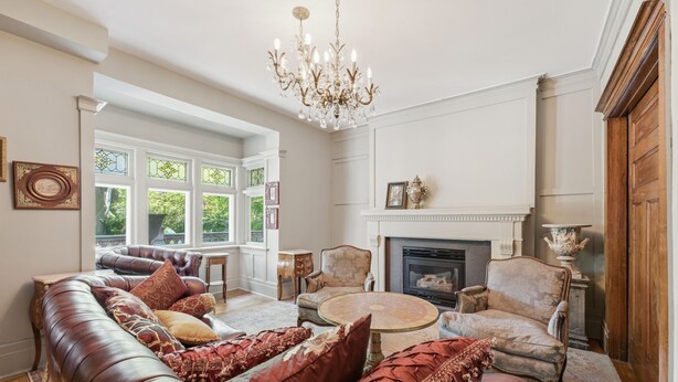 Un salon spacieux avec un canapé en cuir, des fauteuils, une table basse ronde, une cheminée et un lustre.
