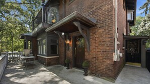 Une maison à deux étages, construite en briques, avec un balcon, une porte d’entrée portant un numéro et un petit jardin.