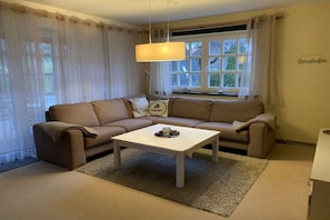 Ein Wohnzimmer mit einem beigefarbenen Sofa, einem weißen Couchtisch und einem Fenster mit Vorhängen.