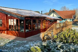 A wooden cabin with a glass enclosure, a wooden staircase, and a snow-covered ground.
