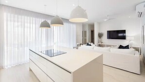 Une cuisine moderne avec un îlot central, des luminaires suspendus, un canapé blanc et un téléviseur à écran plat.