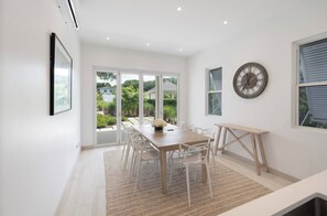 A modern dining area with a wooden table and chairs, a clock on the wall, and large windows offering a view of greenery outside. - #4 Porter's Place - by ZenBreak (Porters)