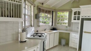 Une cuisine avec des meubles blancs, une cuisinière à gaz, un évier et une poubelle.