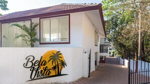 A building with a white exterior, a red roof, and a large window. There is a palm tree and a sign with palm trees and a sun.