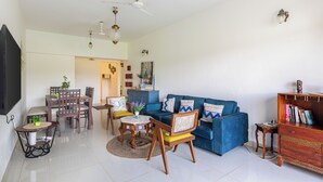A spacious living area with a blue sofa, wooden chairs, a dining table, and a ceiling fan.