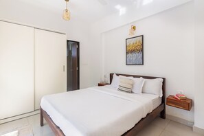 A bedroom with a bed, a nightstand, a wall-mounted shelf, a door, and a ceiling fan.
