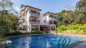 A hotel with a swimming pool, balconies, and lush greenery.