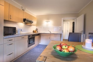 Eine moderne Küche mit Holzschränken, einer Mikrowelle, einem Spülbecken und einem Essbereich mit Tisch und Obstschale.