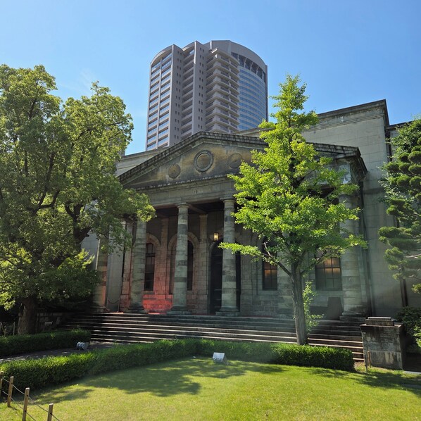 Un edificio storico dall'architettura classica, caratterizzato da colonne e un frontone, circondato da un lussureggiante giardino curato.