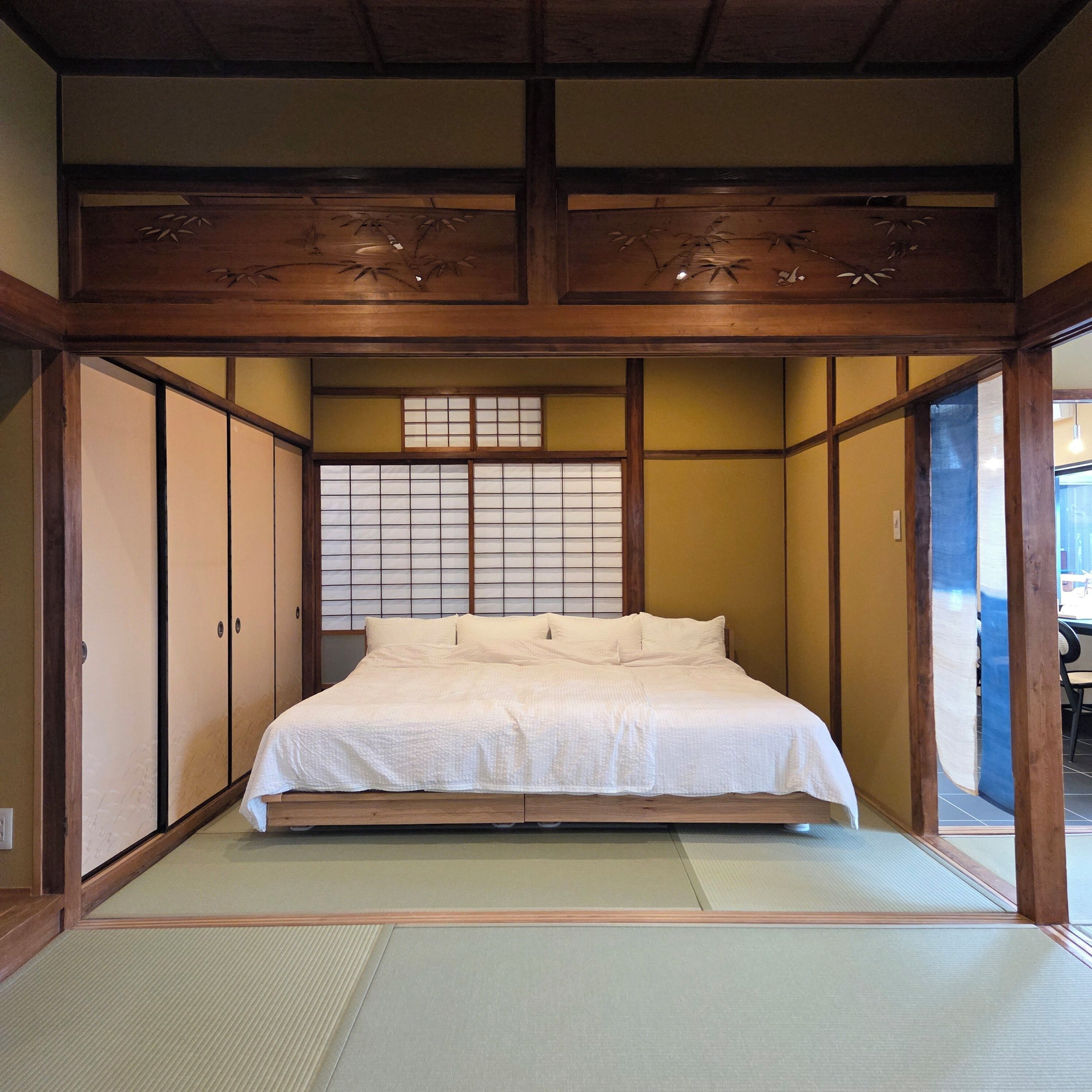 Una habitación tradicional japonesa con suelo de tatami, una cama con ropa blanca, puertas correderas y un mampara de papel shoji.