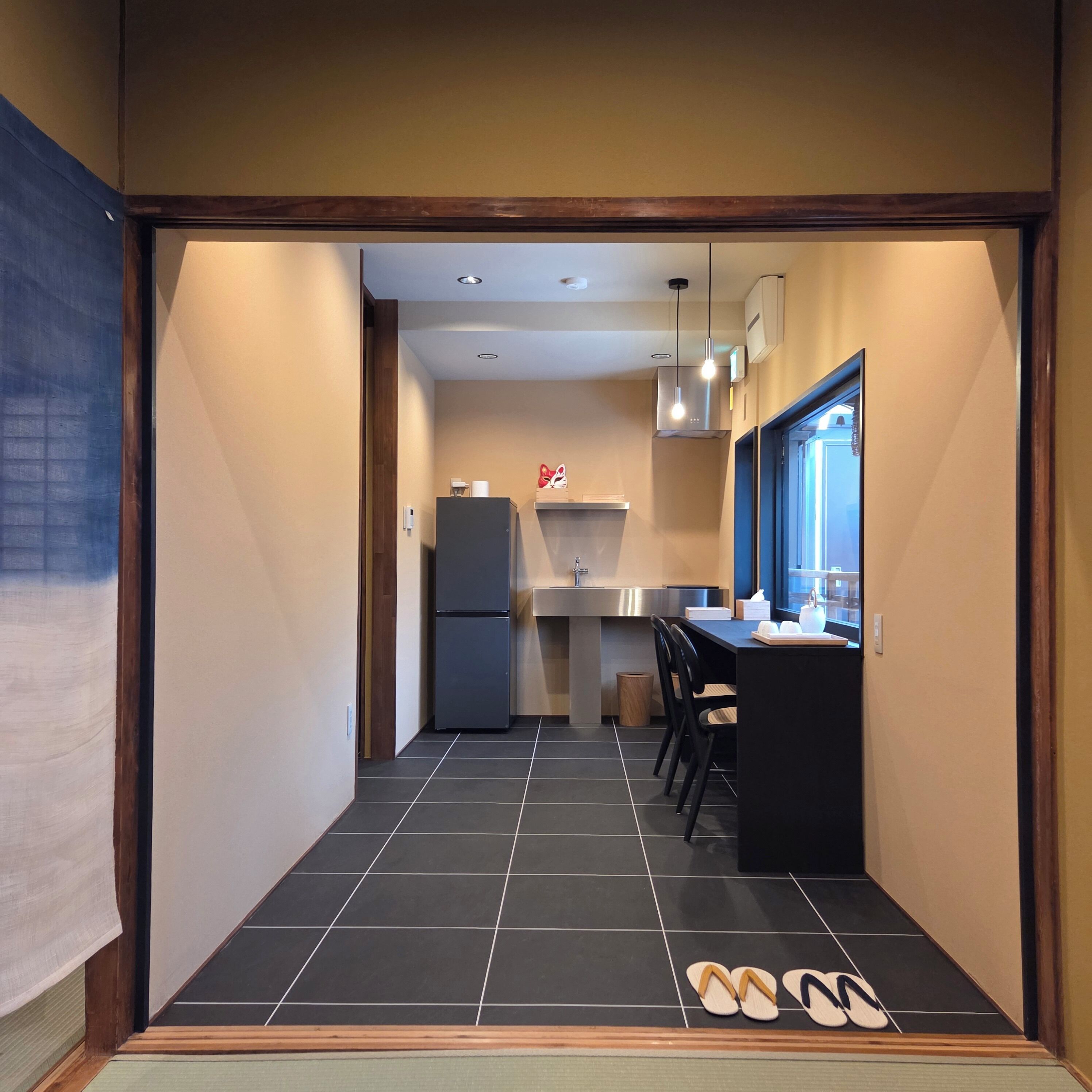 A narrow hallway leading to a kitchen with a refrigerator, a sink, and a window.