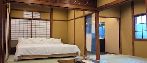 Una habitación japonesa tradicional con suelo de tatami, una cama baja de madera, una mesita con un cuenco y una puerta corredera.