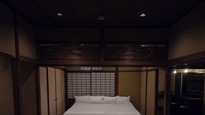 Ein traditioneller japanischer Raum mit Tatami-Böden, einem niedrigen Holzbett, Schiebetüren und einem kleinen Tisch.