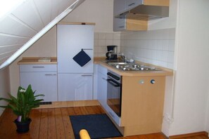Eine kompakte Küche mit weißen Schränken, einem eingebauten Ofen, einer Kaffeemaschine und einem kleinen Spülbecken.
