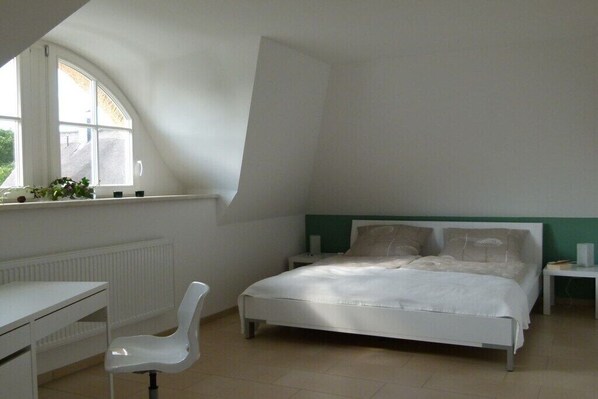 Ein Schlafzimmer mit Bett, Stuhl, Nachttisch, Fenster und Heizkörper.
