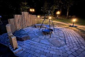 An outdoor patio area with stone flooring, a swing set, and a metal bowl. - Holiday home in Eschede with swimming pool (Eschede)
