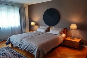 Ein Schlafzimmer mit einem großen Bett, zwei Nachttischen, einer runden Wanddekoration und einem Fenster mit Vorhängen.