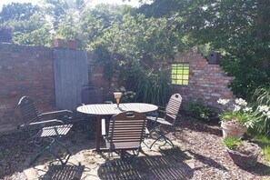 Eine Terrasse mit rundem Tisch und vier Stühlen, umgeben von einer Ziegelmauer und Grünpflanzen.