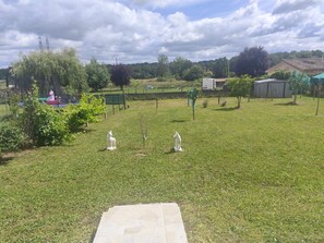 A grassy outdoor area with two white statues, a trampoline, and a fenced playground.