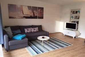 A modern living room with a grey sofa, a round coffee table, a flat-screen TV on a white cabinet, and a bookshelf. - House WalUschi, quiet & close to the beach (Scharbeutz)