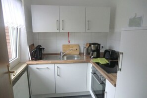 Eine kompakte Küche mit weißen Schränken, einer Holz Arbeitsplatte, einem Spülbecken, einer Kaffeemaschine und einem Wasserkocher.