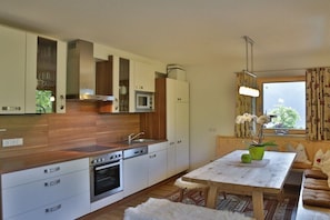 A modern kitchen with a built-in oven, microwave, and sink. There is a dining area with a table and chairs, and a window with curtains. - Holiday apartment with 1 bedroom (Hippach)