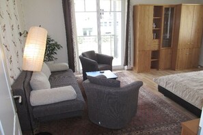 Ein Hotelzimmer mit Sofa, Sessel, Bett, Holzschrank und einem großen Fenster mit Aussicht.