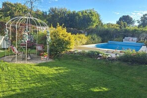 Un jardin avec une piscine, un kiosque et une clôture blanche.
