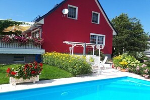 A red house with a swimming pool, white outdoor furniture, and a garden with various flowers. - Knobloch with swimming pool (Seifhennersdorf)