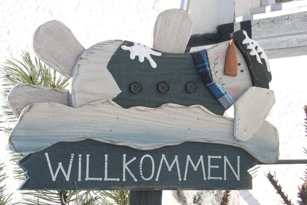 A wooden welcome sign with the word 'WILLKOMMEN' and decorative elements like buttons and a plaid scarf. - Holiday apartment Drexel 1 (Bichlbach)