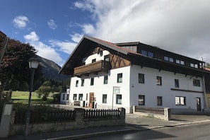A white building with a balcony, a mountain in the background, and a clear sky.